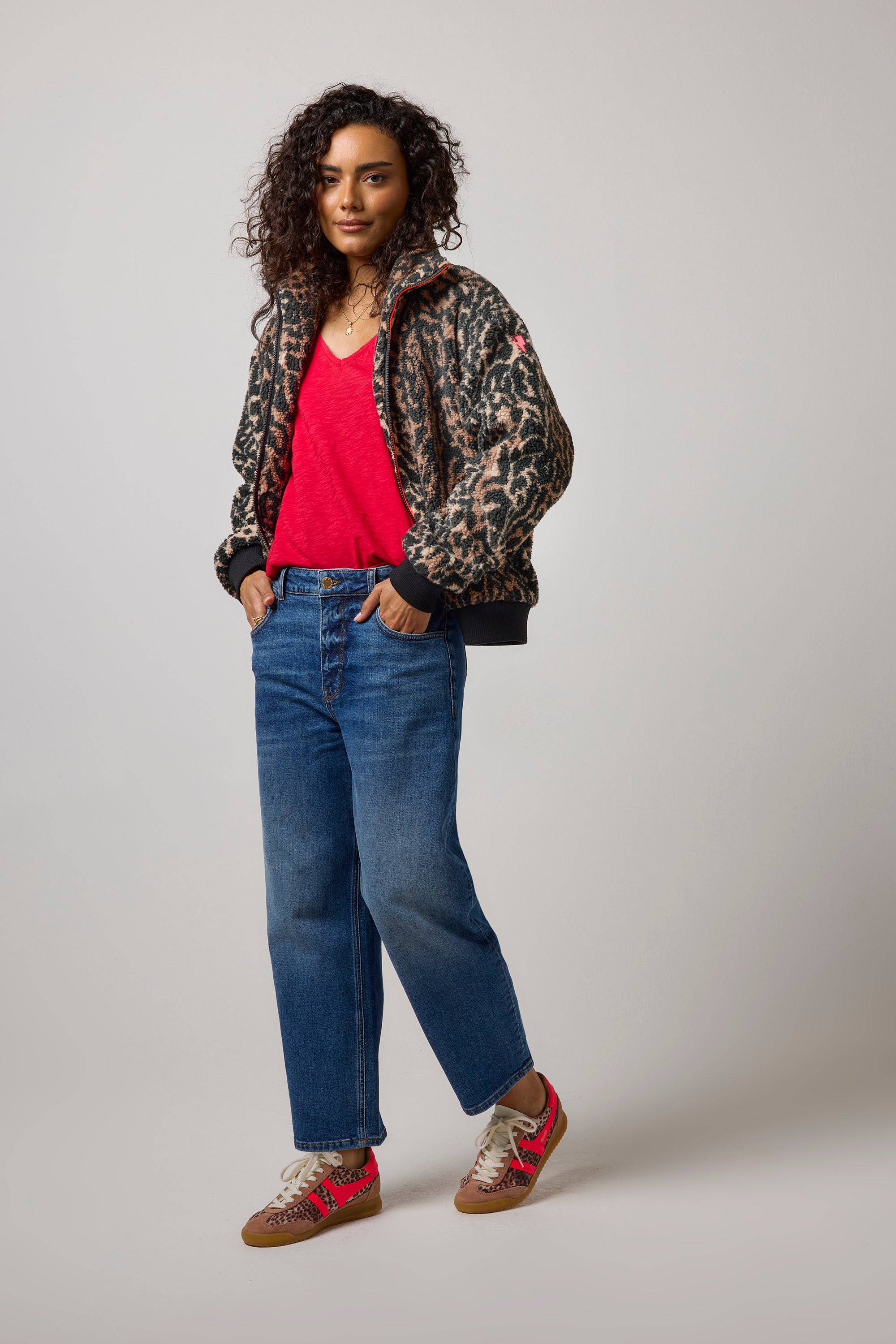 Scamp & Dude Neutral Cloud Leopard Fleece Bomber Jacket | Model wearing a leopard-print bomber jacket over a bright red top and blue jeans