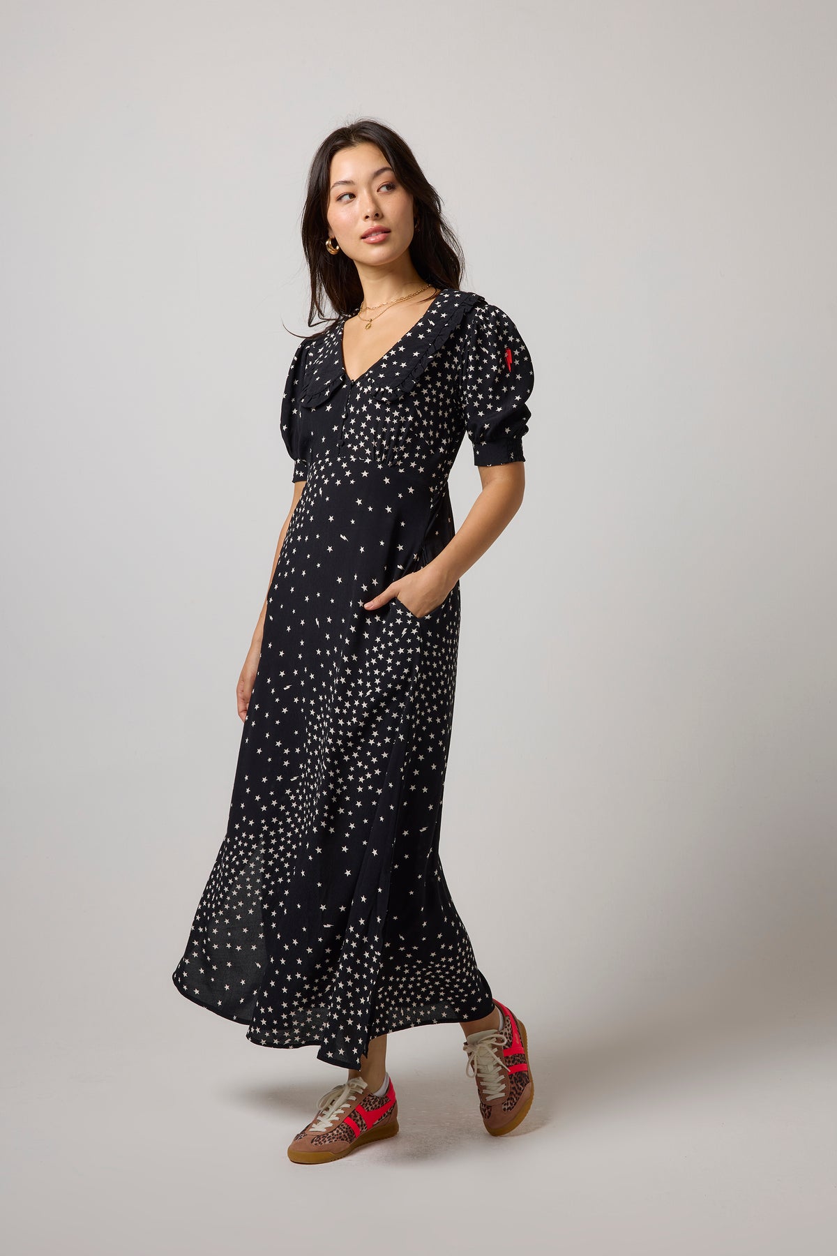 Scamp & Dude Black with White Star Cluster Collared Midi Tea Dress | Model wearing a black midi dress with white star print, featuring puff sleeves, a V-neckline, and side pockets.