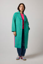 Scamp & Dude Green with Neon Pink Wool Blend Coat | Model wearing a long green wool coat with a neon pink side stripe. Worn with blue jeans and a pair of blue and pink trainers.