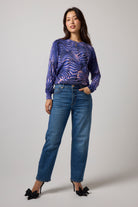 Scamp & Dude Blue Tiger Moth Printed Knit Jumper | Model wearing a long-sleeve blue and purple tiger moth knitted top with a pair of blue jeans.