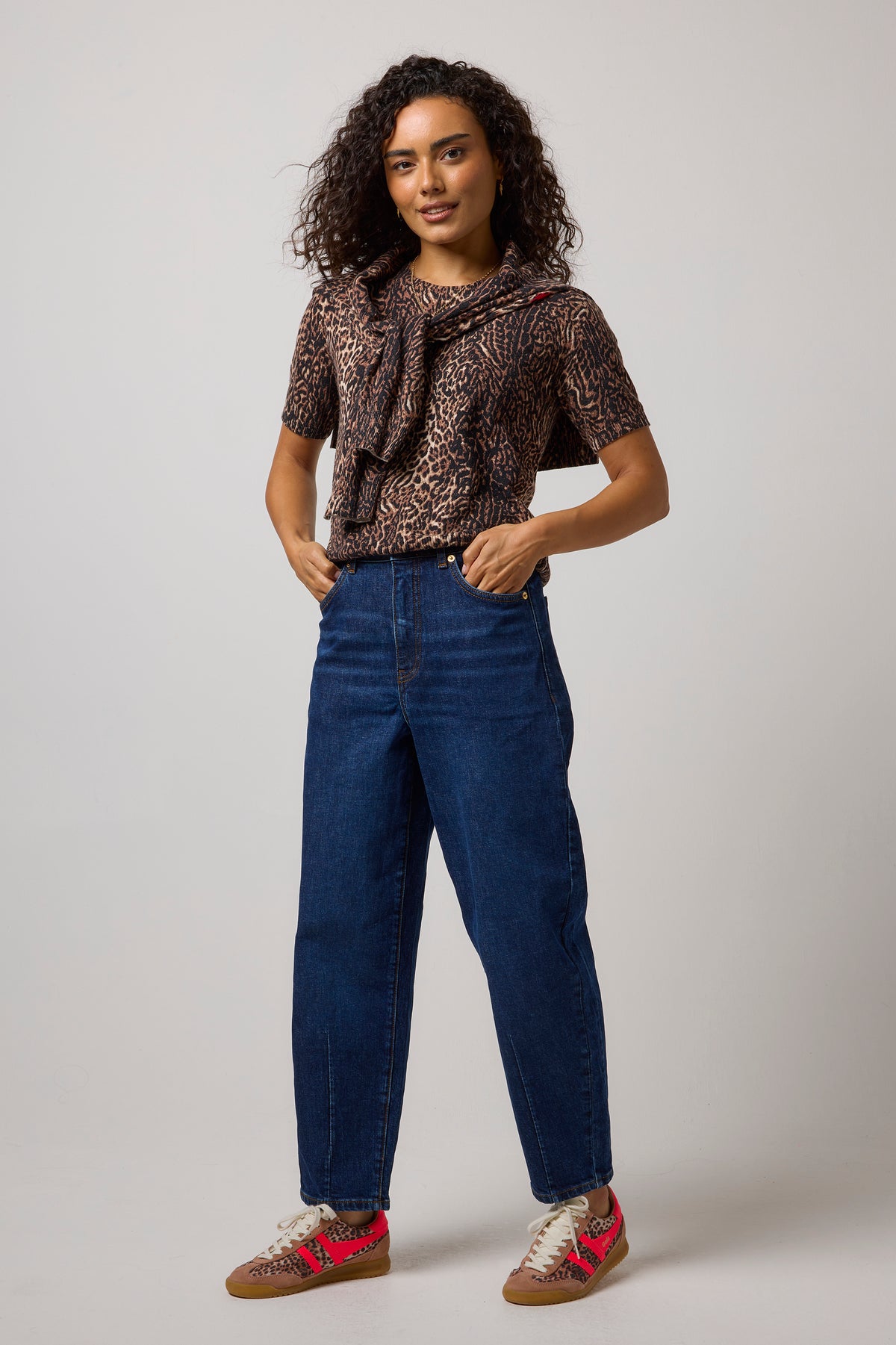 Scamp & Dude Neutral Milano Leopard Short Sleeve Printed Knit Jumper | Model wearing a pair of blue jeans with a leopard print knit top and cheetah print trainers.