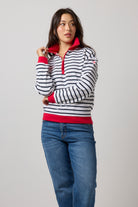 Scamp & Dude Navy Stripe Funnel Neck Sweatshirt | Model wearing a  long-sleeve quarter-zip pullover with navy and white horizontal stripes, accented with bright red trim on the collar and cuffs, paired with blue jeans.
