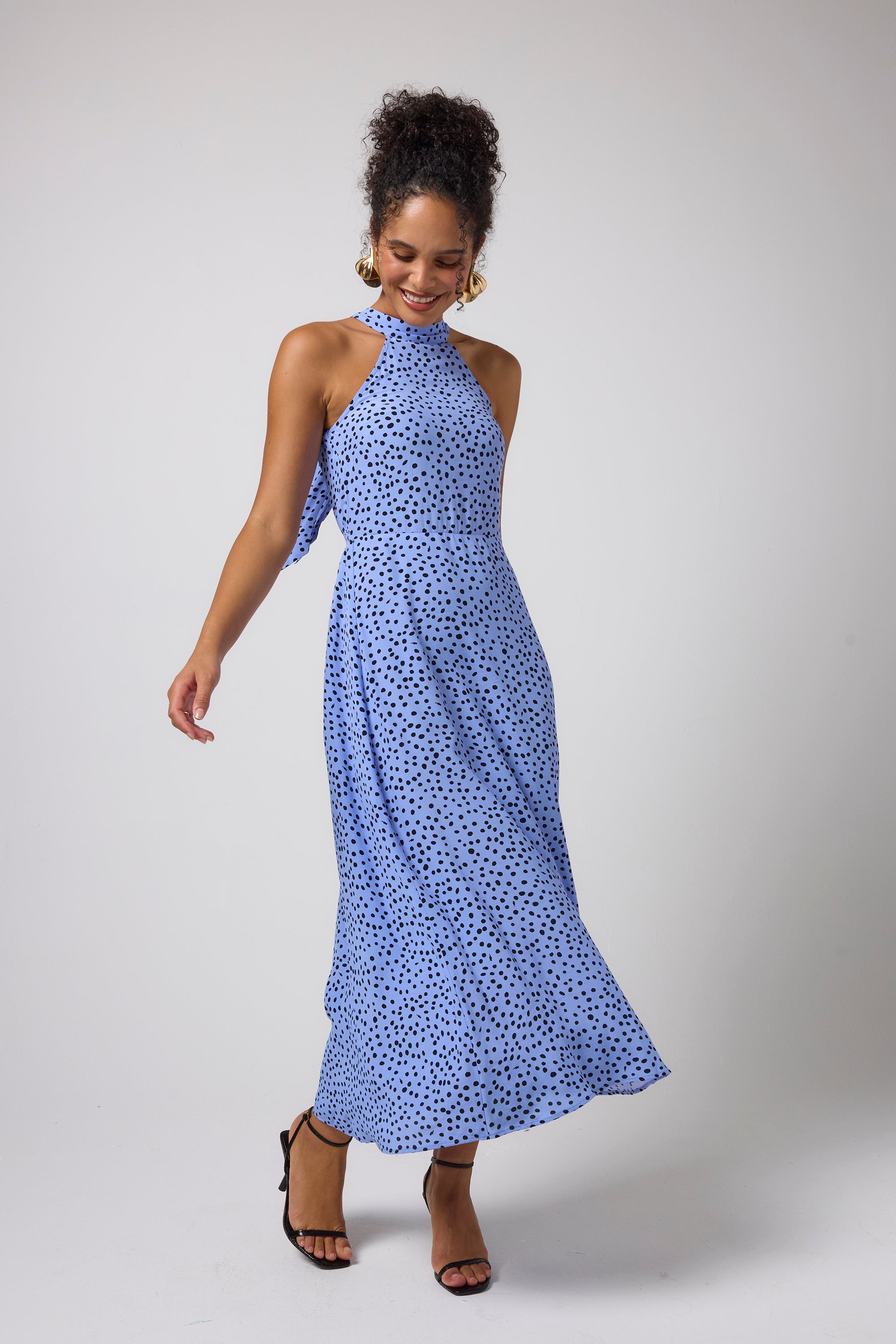 Scamp & Dude Blue with Black Cheetah Spot Halter Midi Dress | Model wearing a sleeveless halter-neck midi dress with a blue and black cheetah spot pattern, paired with black strappy high-heeled sandals.