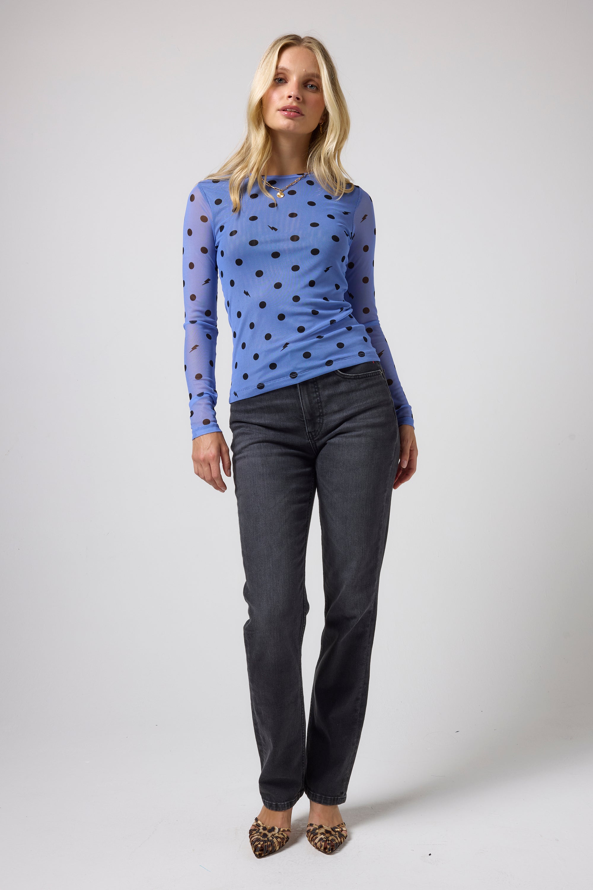 Scamp & Dude Blue Polka Dot Bolt Mesh Top | Model wearing a light blue long-sleeve top with black polka dots, paired with dark grey jeans and leopard-print shoes.