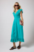 Scamp & Dude Turquoise Broderie Shirred Midi Dress | Model wearing a turquoise midi dress with broderie sleeves and a smocked bodice. Paired with black strappy sandals and tortoise shell sunglasses.