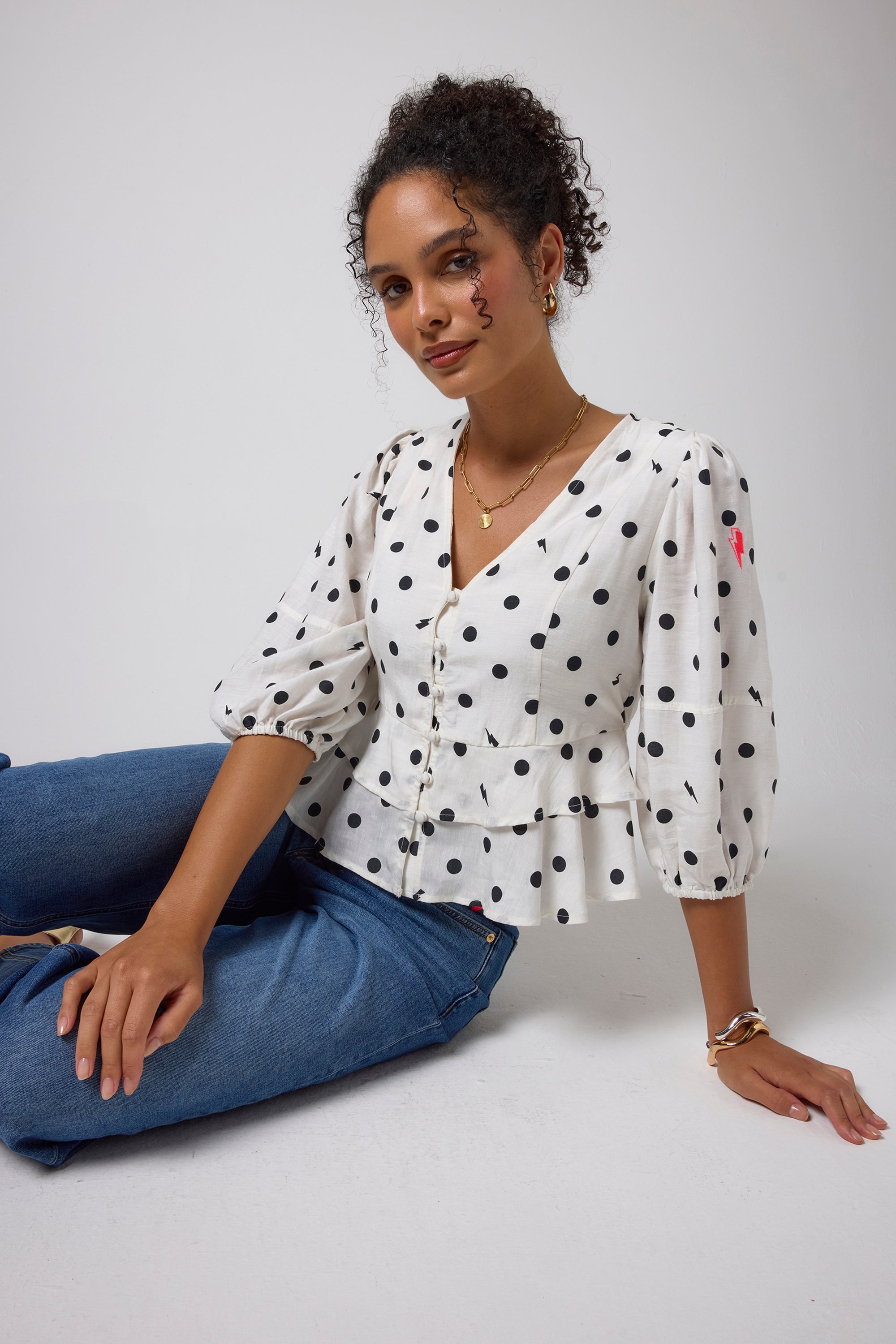 Scamp & Dude Ivory with Black Polka Dot Bolt Peplum Blouse | Model wearing an ivory blouse with black polka dots and blue jeans.