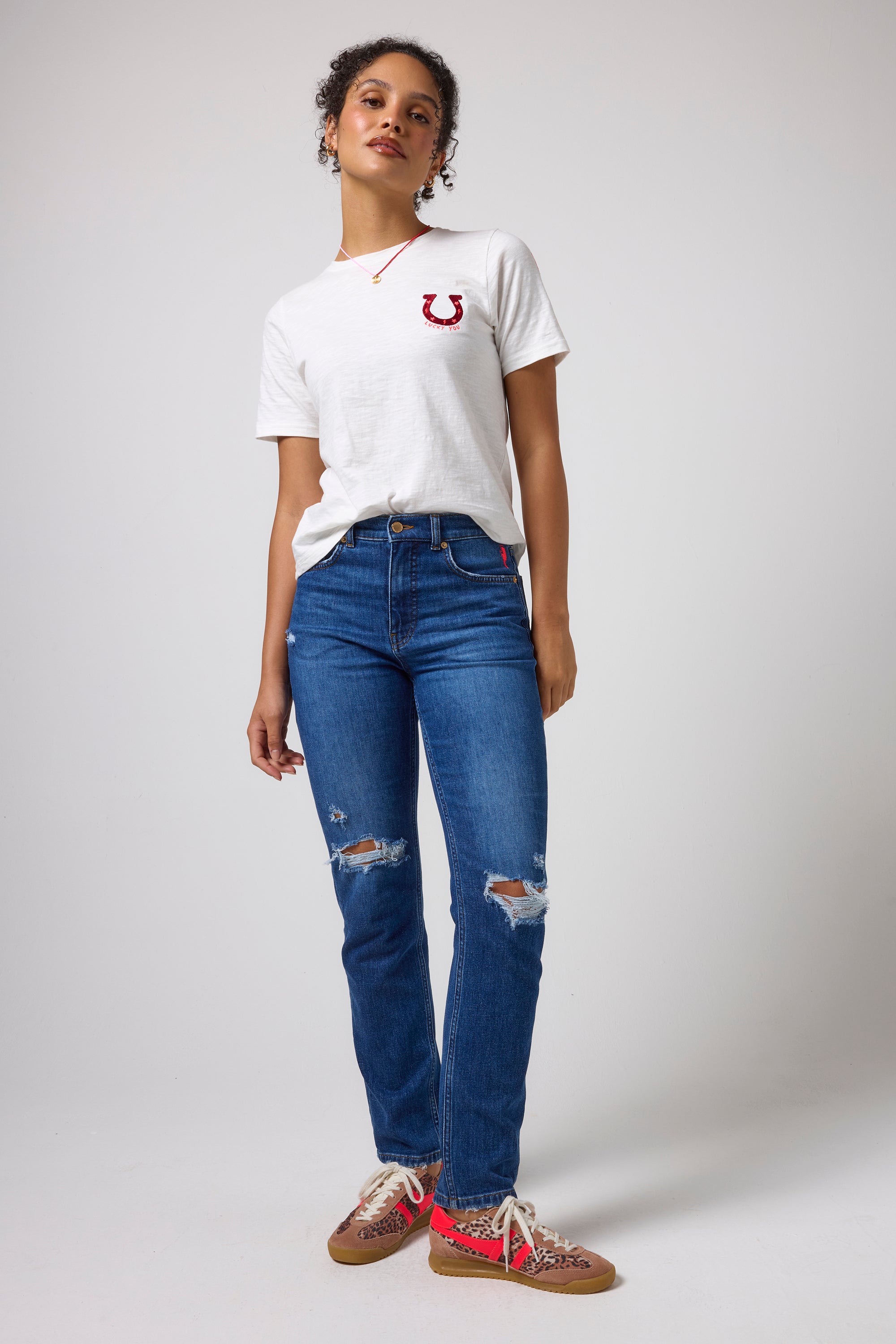 Scamp & Dude White Lucky You T-Shirt | Model wearing a white crewneck t-shirt with a red embroidered logo on the chest, paired with blue distressed jeans.