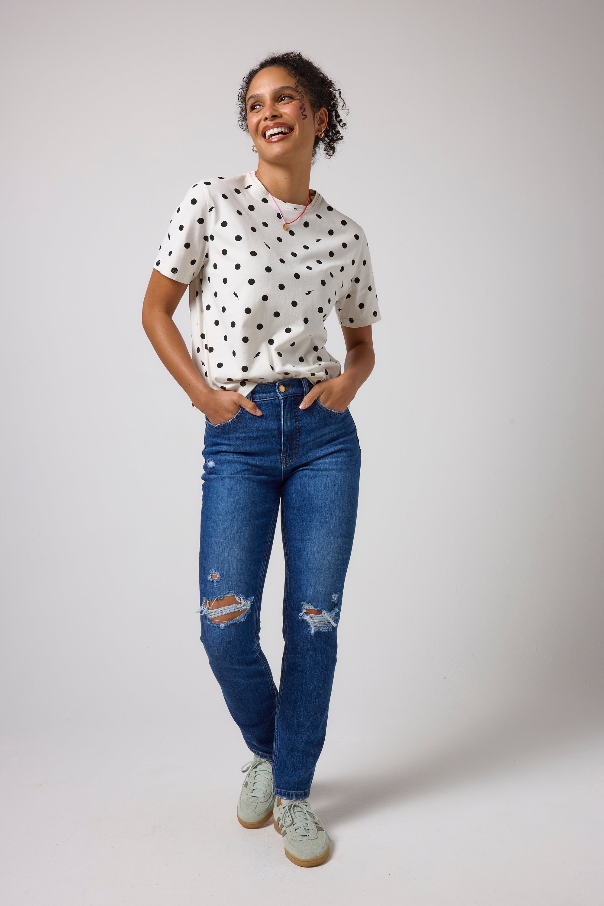 Scamp & Dude Ecru Polka Dot Bolt Classic T-Shirt | Model wearing a white short-sleeve t-shirt with black polka dots, paired with blue distressed jeans and light green trainers.