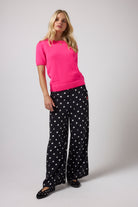 Scamp & Dude Black with White Polka Dot Bolt Wide Leg Trousers | Model wearing a pink knit top with a pair of black and white polka dot trousers.
