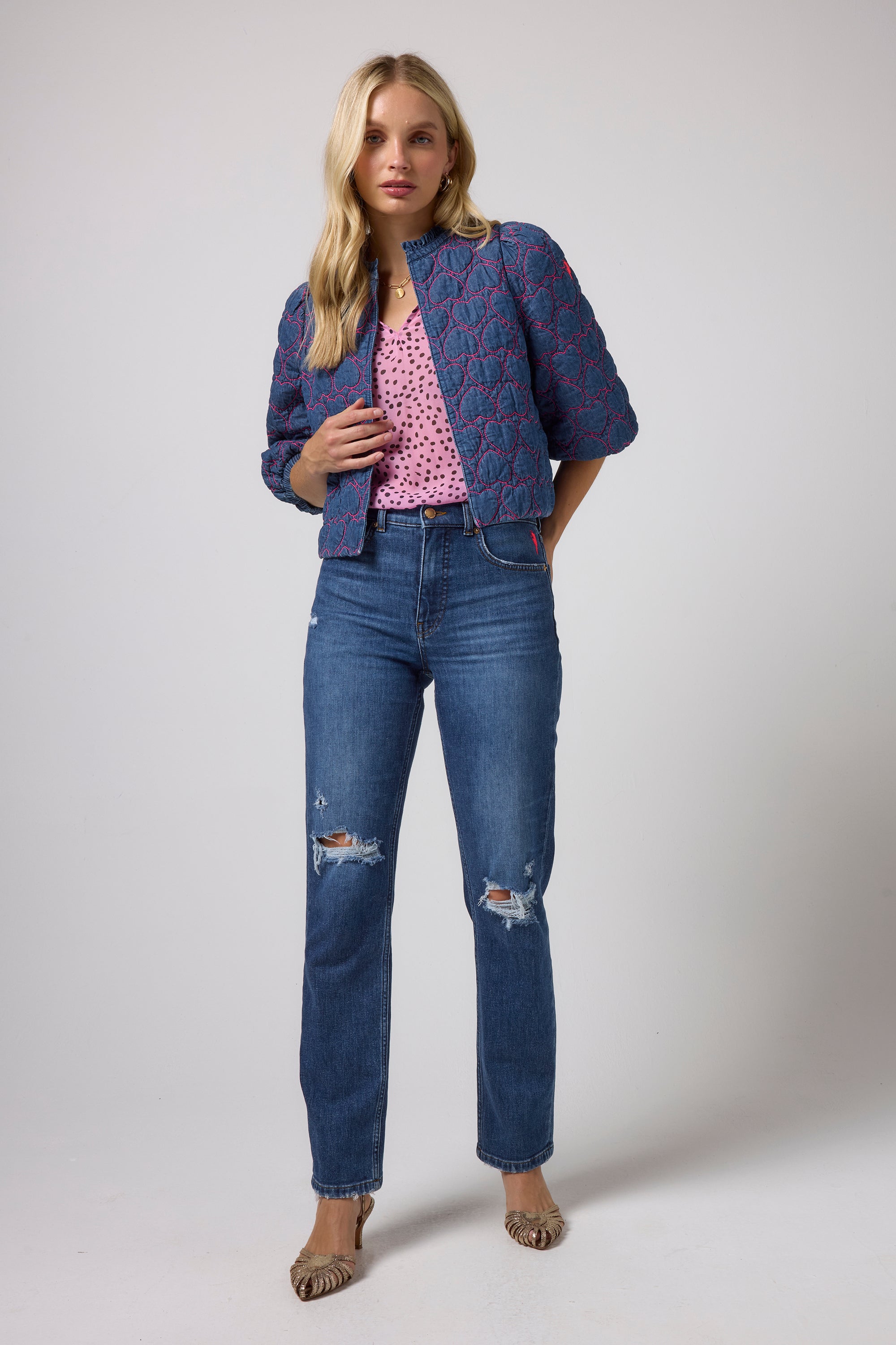 Scamp & Dude Blue Denim Quilted Heart Jacket | Model wearing a blue quilted denim jacket over a pink polka-dot top and blue distressed jeans.