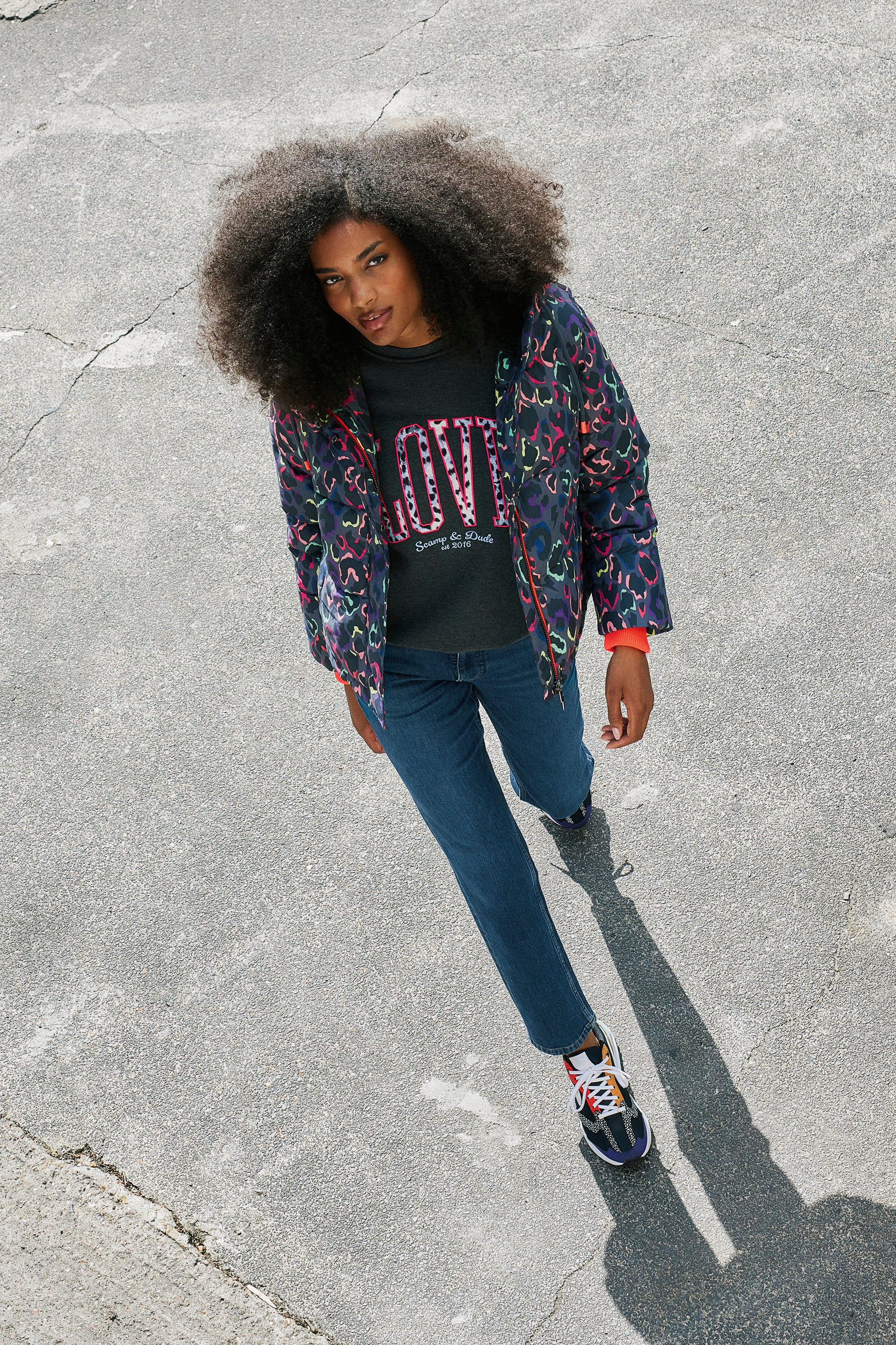 Scamp and Dude Grey with Rainbow Shadow Leopard Short Puffer Coat | Model wearing blue jeans with a dark grey love sweatshirt and a grey rainbow leopard puffer coat.