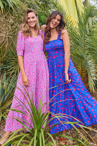 A lady wearing a soft blue with coral floral leopard maxi dress hugging a friend wearing a different Scamp & Dude dress