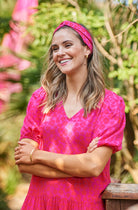 A lady wearing a magenta with hot pink floral leopard and lightning bolt print headband with a matching dress