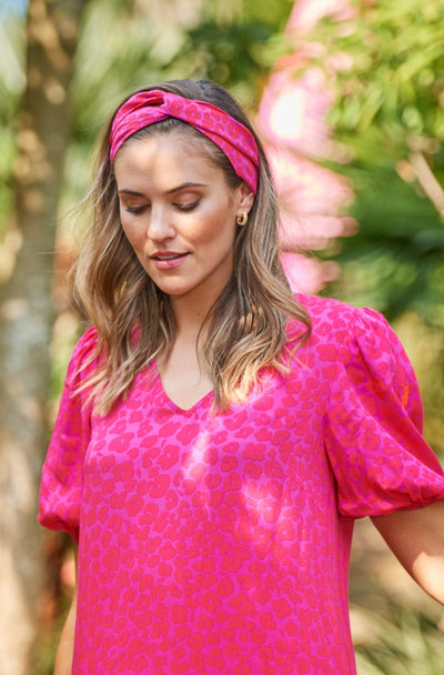 A lady wearing a magenta with hot pink floral leopard and lightning bolt print headband with a matching dress