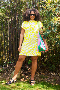 A curly-haired lady wearing an oversized blush with yellow leopard and lightning bolt print T-shirt dress with sandals