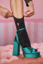 Scamp and Dude Black and Gold Leopard Ray Lurex Jacquard Socks | Model wearing a pair of black and gold leopard ray lurex socks with green high heels.