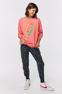 Scamp and Dude Coral with Rainbow Lightning Bolt Oversized Sweatshirt | Model smiling wearing coral sweatshirt with lightening bolt on the front with grey leopard print leggings with white trainers