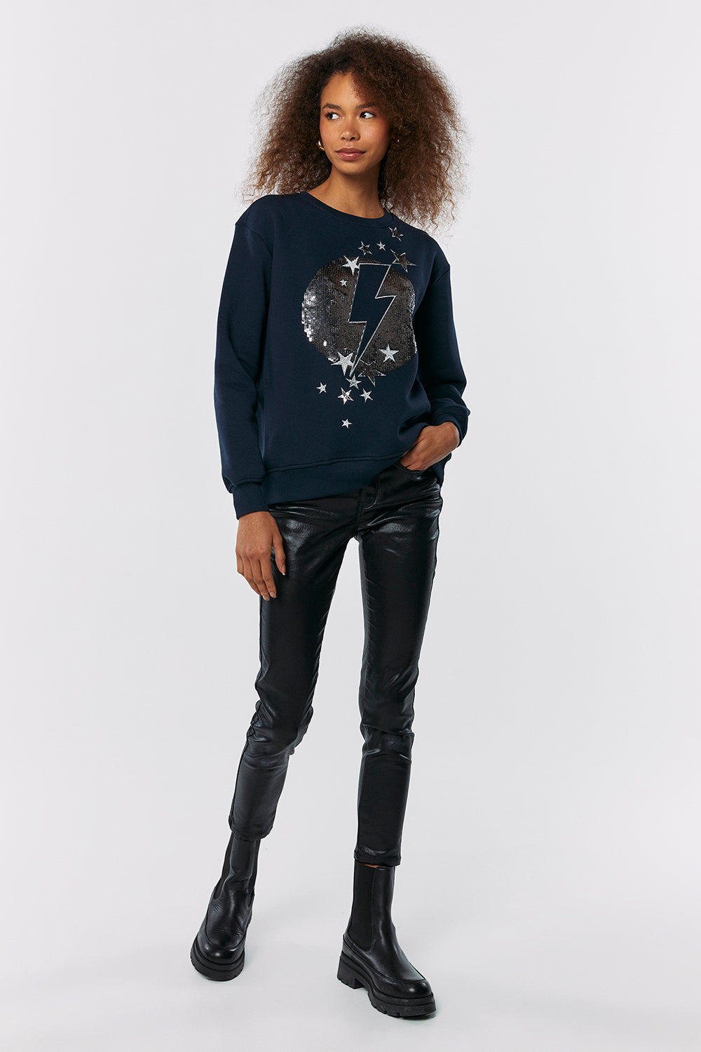 Scamp and Dude Navy with Sequin Lightning Bolt Oversized Sweatshirt | Model with hand in pocket wearing a navy sweatshirt with sequin moon with lightening bolt printed on the front with leather trousers and black boots 