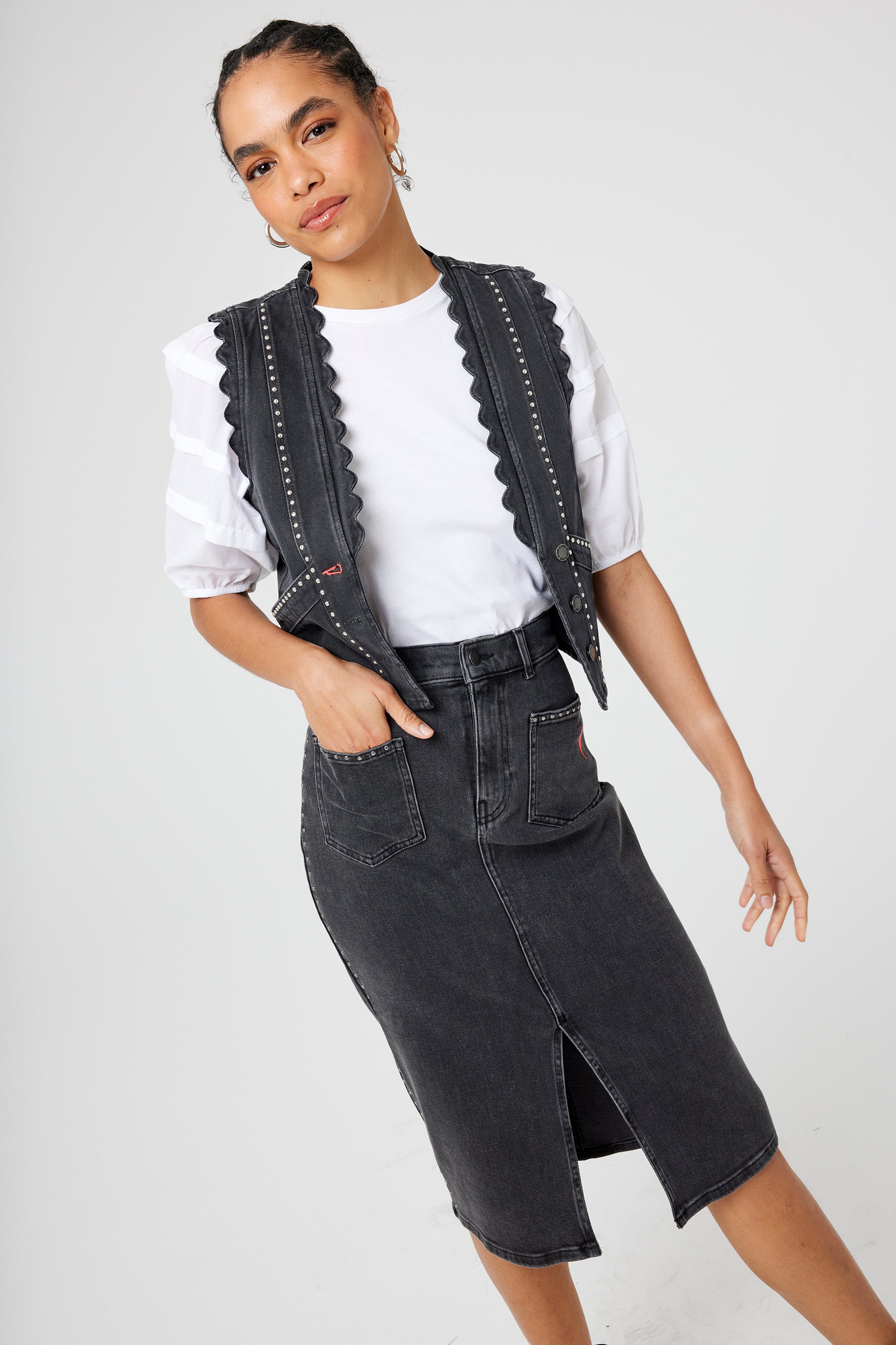 Scamp and Dude Washed Black Studded Denim Split Front Midi Skirt | Model wearing a washed black denim midi skirt featuring stud detail and front split, paired with a white t shirt and matching denim waistcoat.