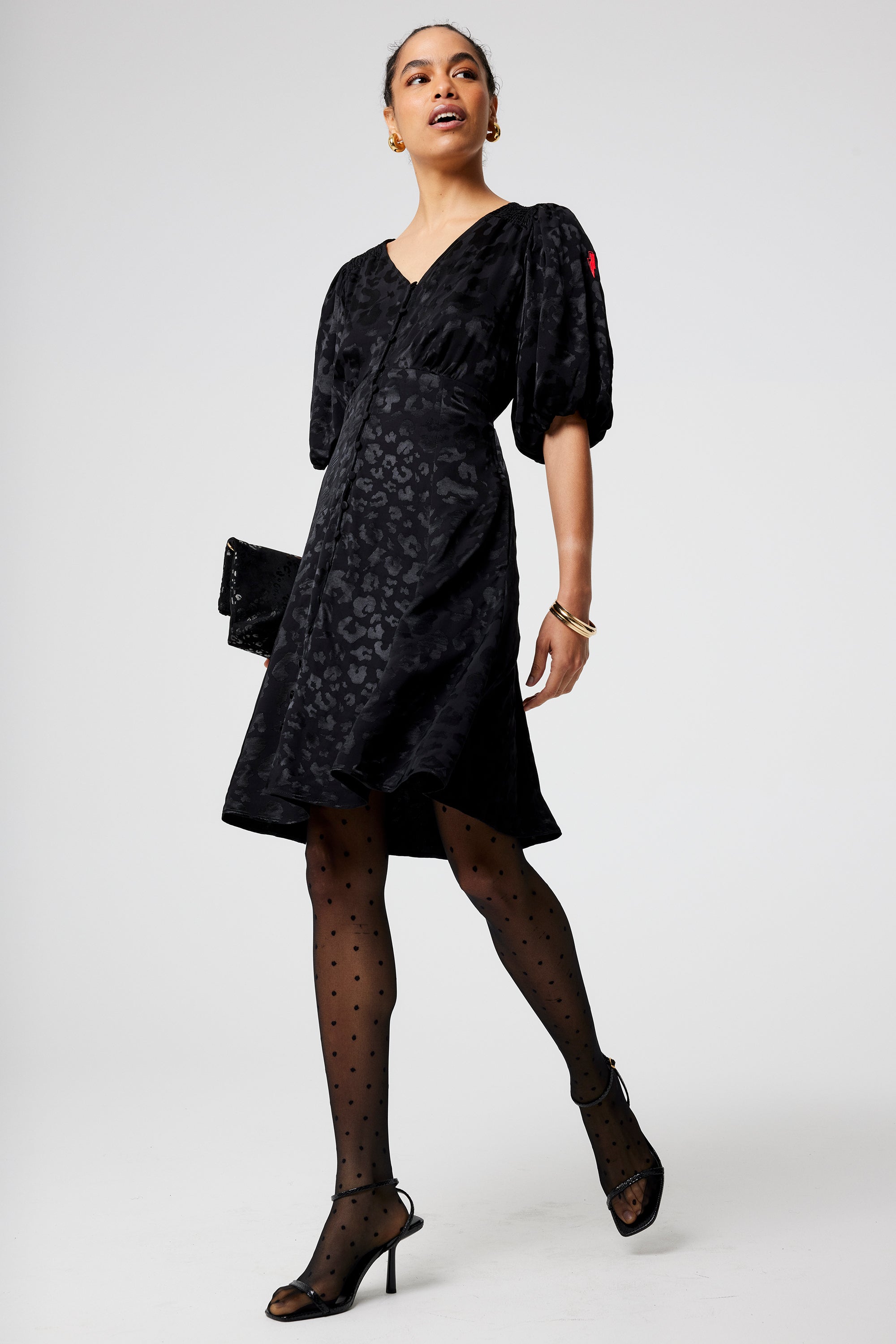 Scamp and Dude Black Jacquard Leopard Puff Sleeve Short Tea Dress | Model wearing a short v neck black tea dress in a leopard jacquard finish paired with black tights and heels.