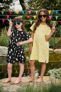 Two girls wearing T-shirt dresses, one is blush with neon yellow leopard, the other is black with white lightning bolts