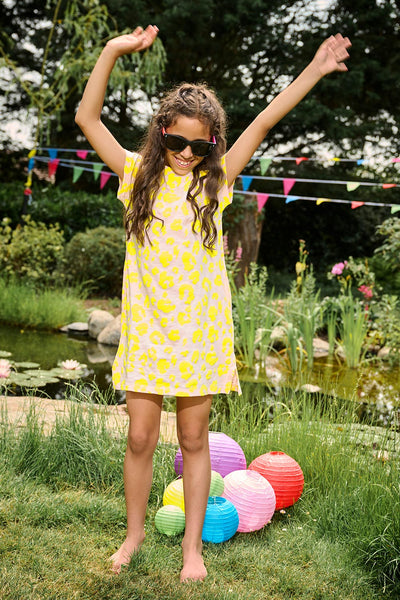 A girl with her arms up in the air wearing a blush with neon yellow leopard and lightning bolt T-shirt dress