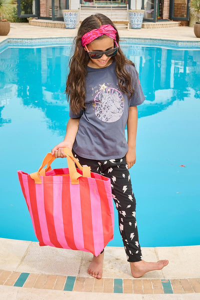 Scamp and Dude | Kids Snow Leopard Oversized Band T-Shirt | Young girl wearing a grey t-shirt holding a pink striped tote bag and lightening bolt leggings in front of a swimming pool