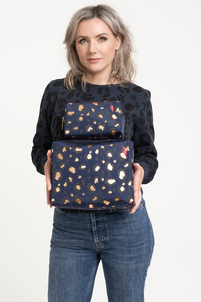 Scamp & Dude x Sali Hughes Blue with Black and Gold Foil Snow Leopard Cosmetic Bag | Sali Hughes holding two black and gold cosmetic bags wearing jeans and leopard print grey top