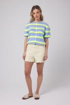 Scamp and Dude Light Blue with Yellow Stripe Short Sleeve Cardigan | Model wearing a pale blue and yellow stripe short sleeve cardigan with a pair of yellow scallop denim shorts.