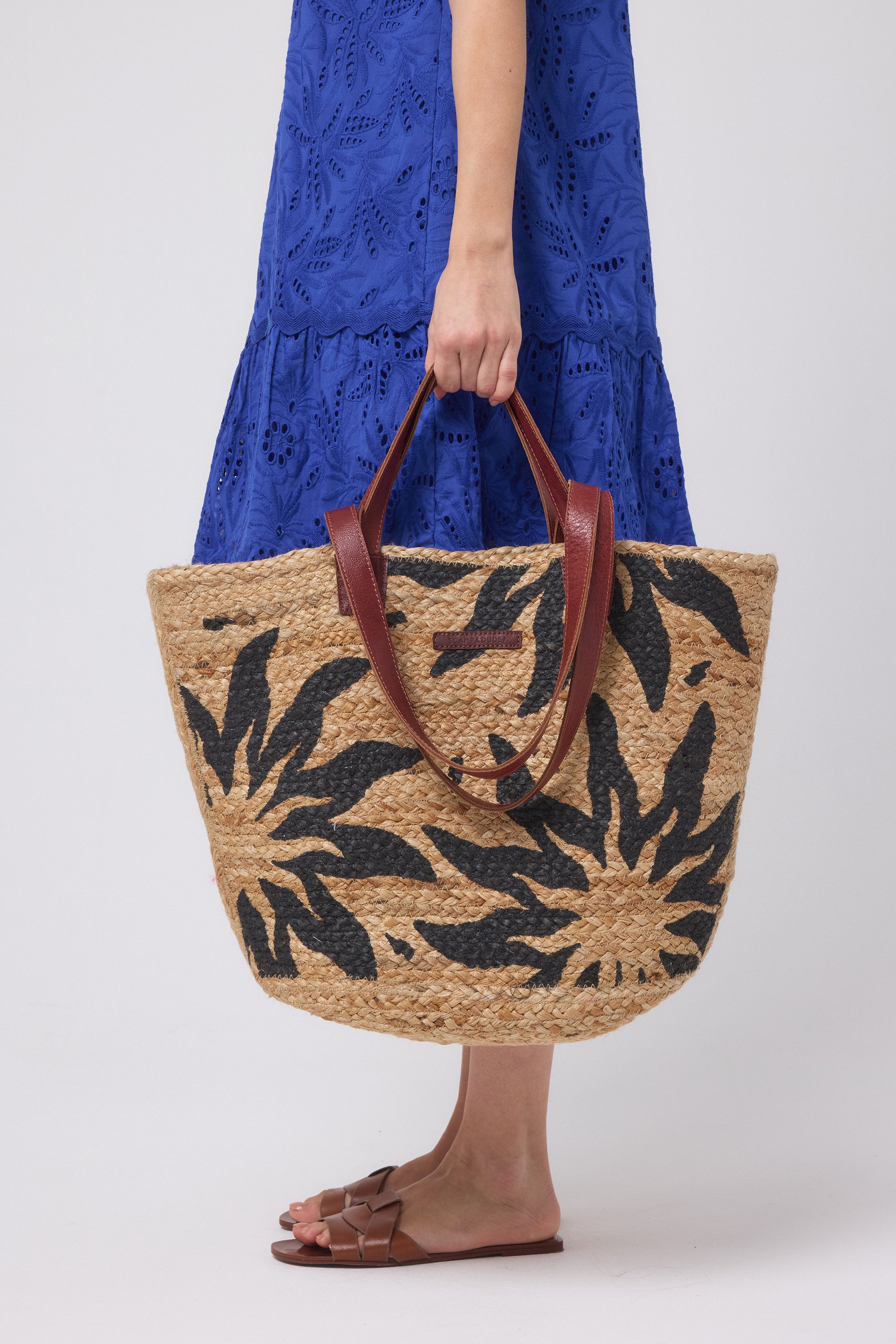 Scamp and Dude Natural with Black Sun Straw Basket Bag | Model wearing a blue broderie dress holding a straw bag with black sun design on it.