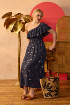Scamp & Dude Navy with Gold Foil One Shoulder Midi Dress | Model in a navy one-shoulder dress featuring foil print with a ruffle shoulder detail.