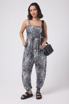 Scamp and Dude Grey with Black Cheetah Jersey Jumpsuit | Model wearing a grey and white cheetah print jumpsuit with a black cross body bag. Worn with black studded sandals.