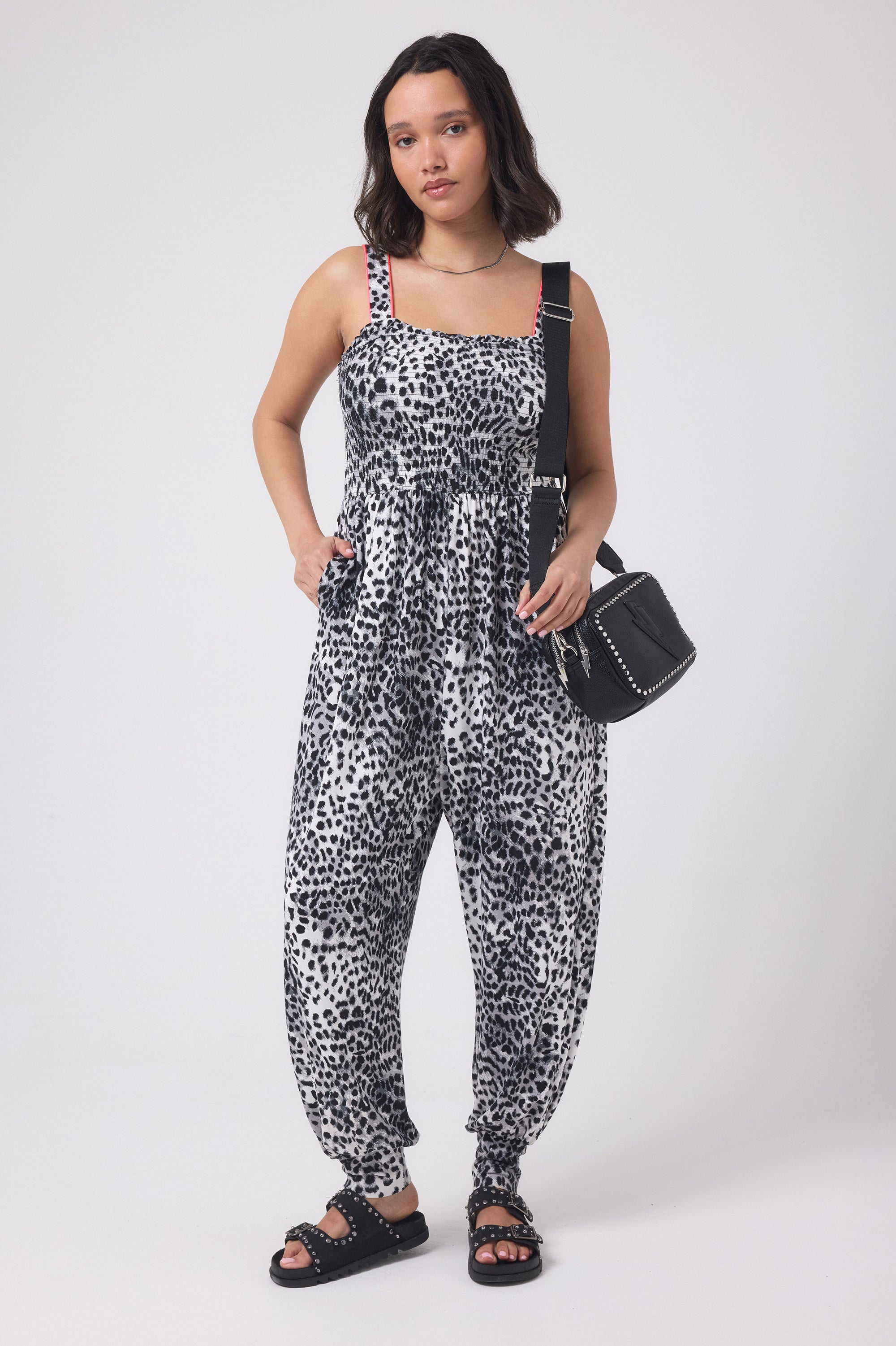 Scamp and Dude Grey with Black Cheetah Jersey Jumpsuit | Model wearing a grey and white cheetah print jumpsuit with a black cross body bag. Worn with black studded sandals.