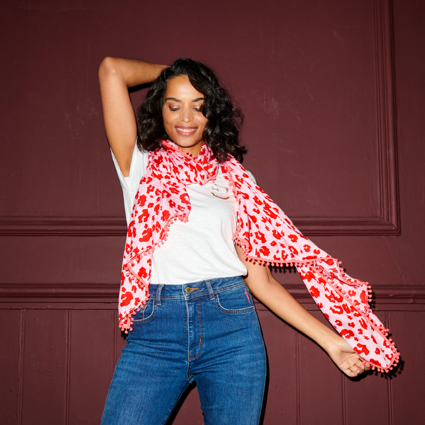 Scamp and Dude | Model looking down with one hand behind her head and one hand holding a pink and red leopard print scarf with blue jeans and a white shirt