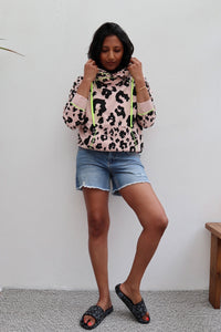 A lady wearing a pale peach with black mixed leopard and lightning bolt cowl neck hoodie with  denim shorts