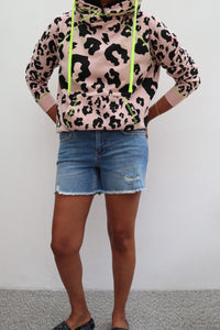 A lady wearing a pale peach with black mixed leopard and lightning bolt cowl neck hoodie with denim shorts