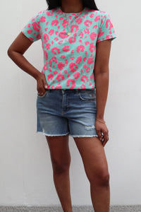 A lady wearing a green with neon pink leopard and lightning bolt print T-shirt with denim shorts