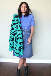 A lady wearing a blue t-shirt tucked into a midi indigo denim skirt with a chunky green & black zebra knitted cardigan