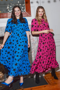 Two women wearing matching star & lightning bolt dresses in different colourways, one is magenta, the other is blue