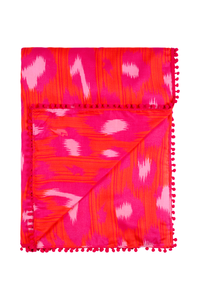 A folded red with hot pink and pale pink leopard ikat and lightning bolt print scarf with a pink pom pom trim 