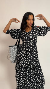 A lady wearing a black with white star maxi dress holding a silver metallic overnight bag with lightning bolt quilting detail
