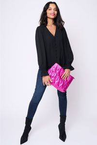 A lady wearing a black blouse & dark indigo jeans holding a metallic hot pink swag bag with quilted lightning bolts