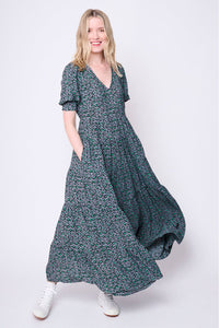 A blonde lady swishing the skirt of her grey with black and green snow leopard and lightning bolt print v-neck maxi dress