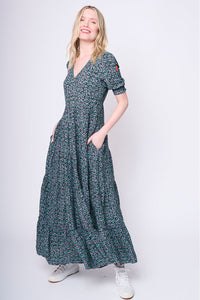 A blonde lady with her hands in her pockets wearing a black and green snow leopard and lightning bolt print v-neck maxi dress