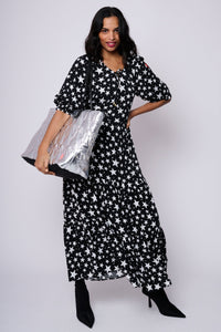 A lady wearing a black with white star maxi dress holding a silver metallic overnight bag with lightning bolt quilting detail