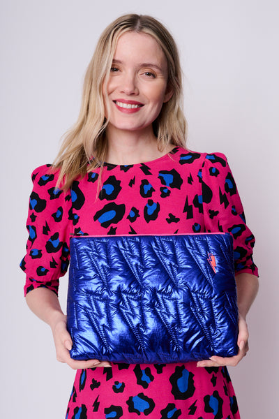 A lady holding a metallic electric blue swag bag with quilted lightning bolt detail & a neon pink embroidered lightning bolt