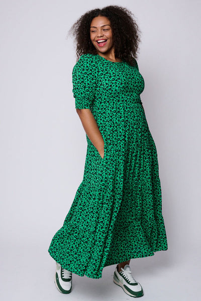 Scamp and Dude Bright Green Leopard Tiered Maxi Dress | Model with curly hair wearing long green leopard print dress and white and green trainers
