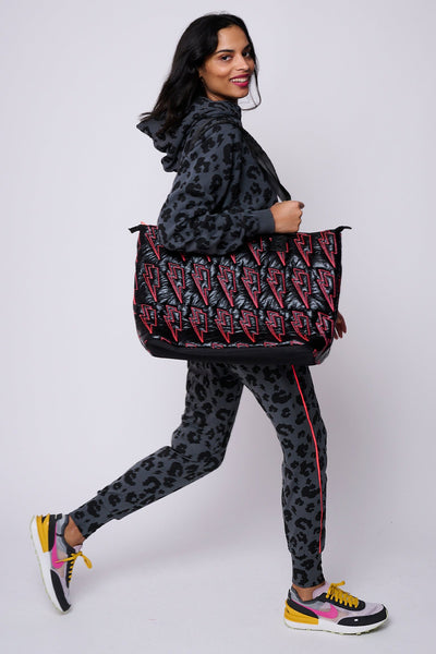A lady in Scamp & Dude loungewear holding a black metallic overnight bag with neon coral lightning bolt quilting detail