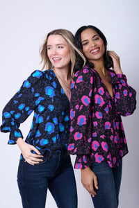 Two women wearing matching snow leopard, star and lightning bolt print tops in different colourways
