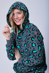 A lady smiling with her hood up wearing a grey with green & black snow leopard and lightning bolt print hoodie